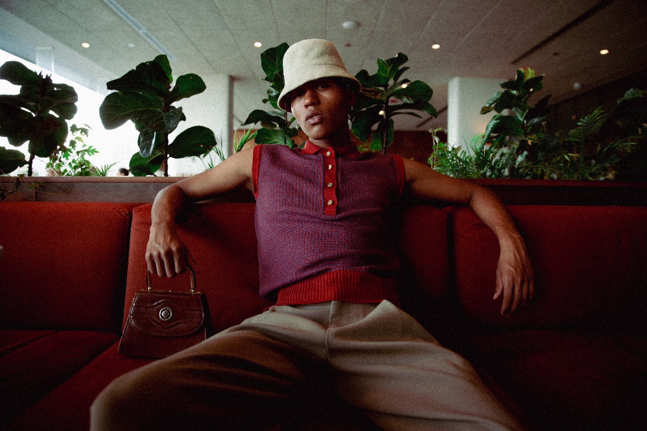A stylish person sitting on a sofa, wearing a hat and trendy outfit, holding a handbag, embracing sustainable fashion