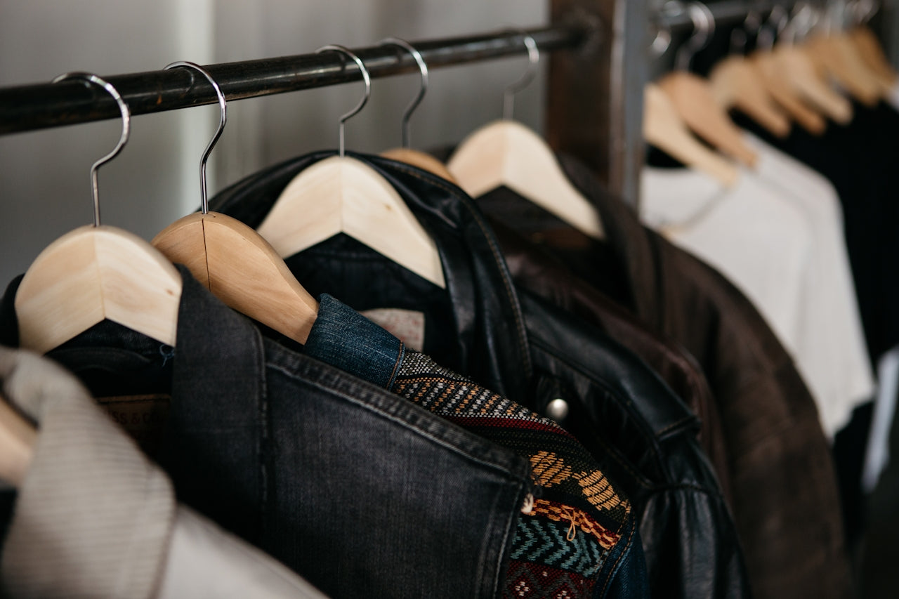 Stylish preloved fashion pieces, including jackets, blazers, and colorful t-shirts, hung on an open wardrobe rack.Stylish preloved fashion pieces, including jackets, blazers, and colorful t-shirts, hung on an open wardrobe rack.
