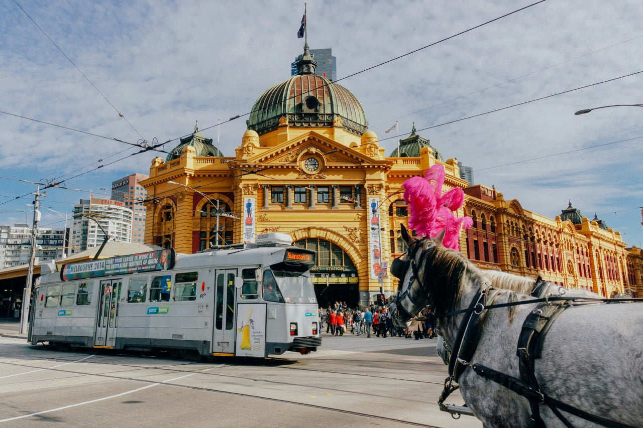 A lively street scene in Melbourne featuring the historic Flinders Street Station with its iconic yellow facade.